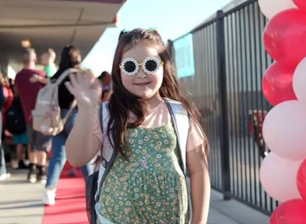 Little girl in sunglasses waves at camera