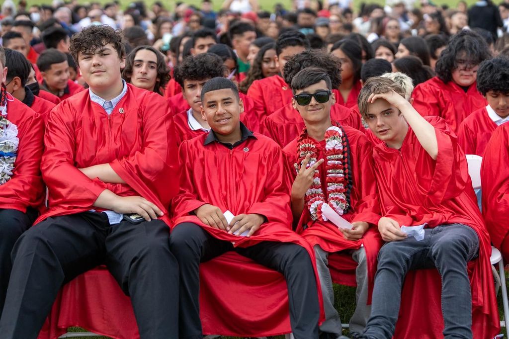 Student graduates sitting down wearing red gowns.