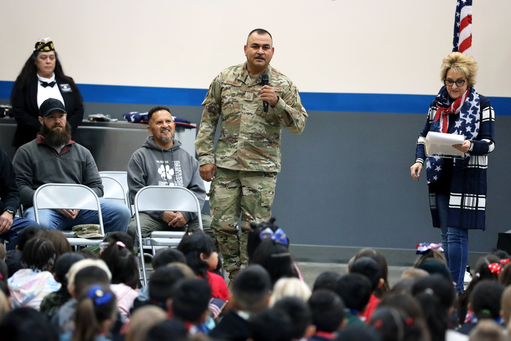 Male veteran in fatigues addresses students at school tribute