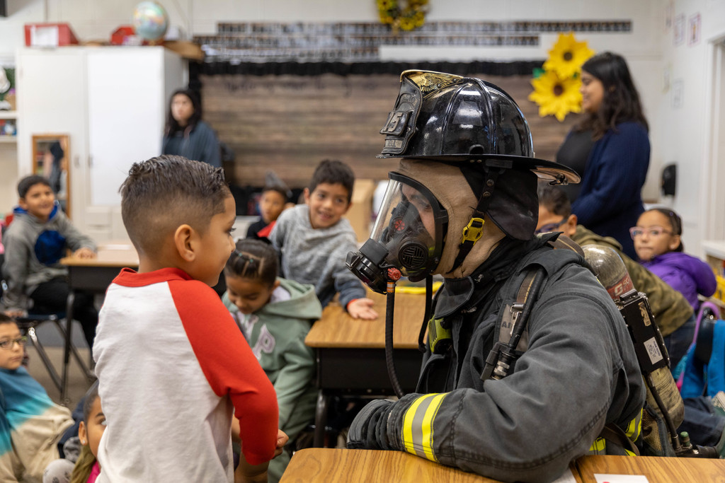 Firefighter in full gear talks to first-grade student