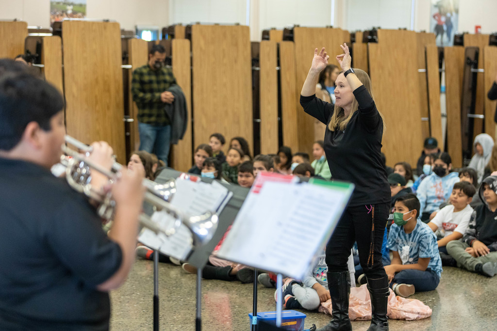 Music teacher Beth Holtan directs student playing trumpet in front of elementary assembly