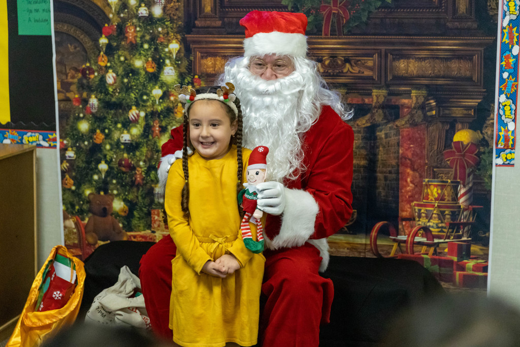 Little girl in yellow dress, reindeer headband receives elf doll from Santa