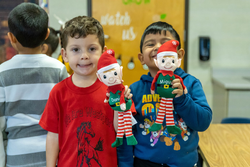 Little boy in red shirt and second little boy in blue shirt hold up elf dolls