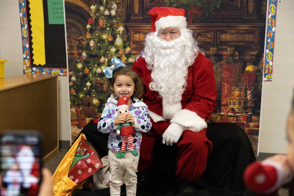 Little girl with blue hair bow and elf doll poses with Santa