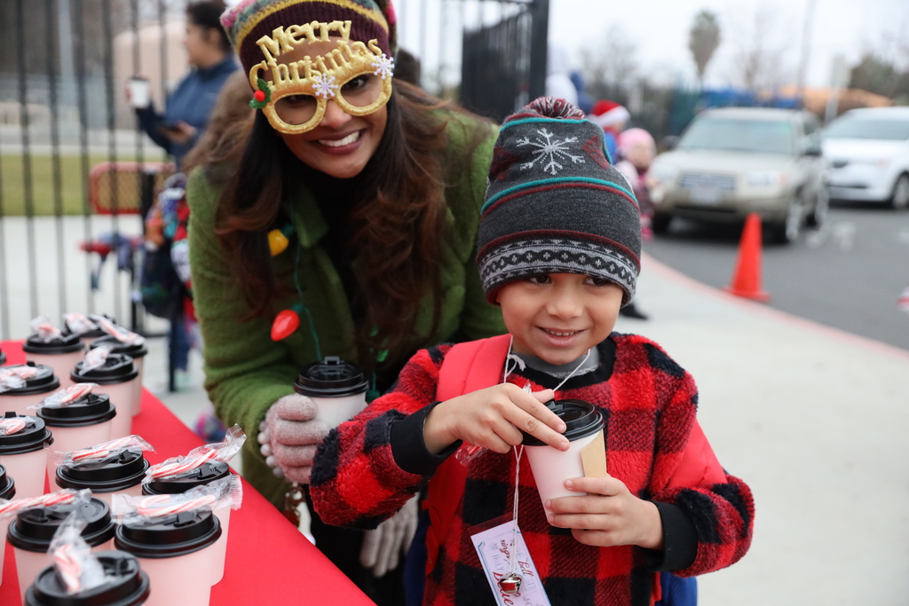 Principal Arti Narayan smiles next to a young boy in a knitted beanie holding hot cocoa