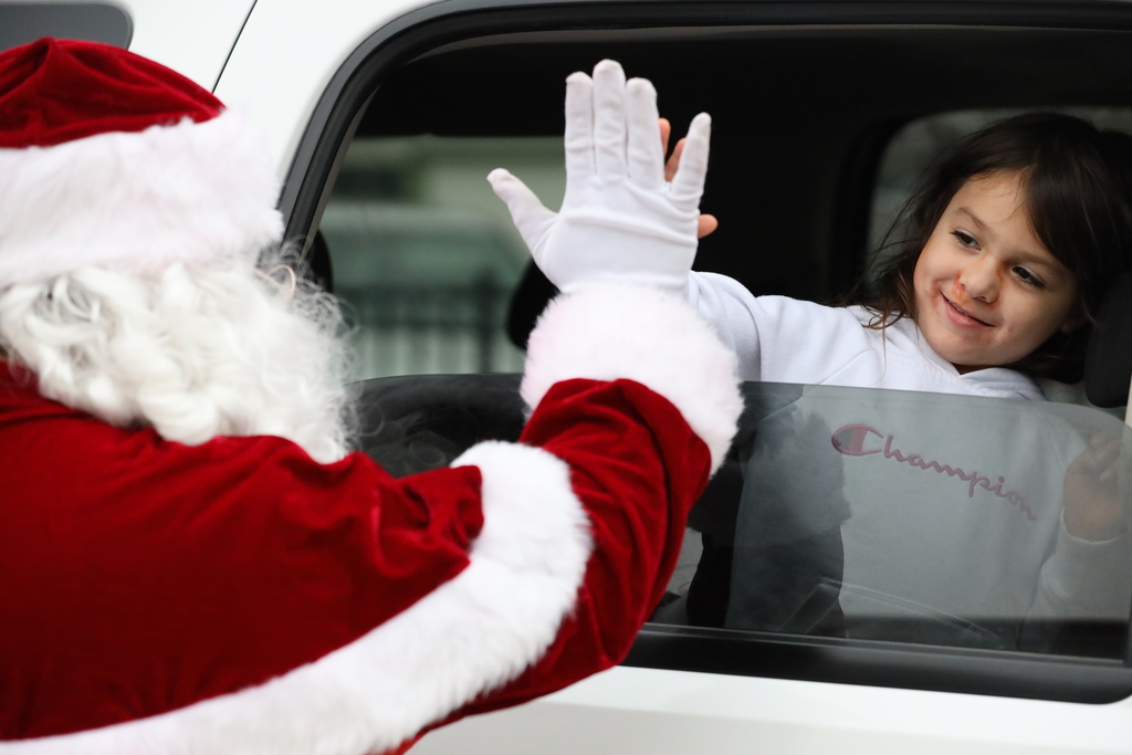 Santa high-fives a little girl through the window of a white car