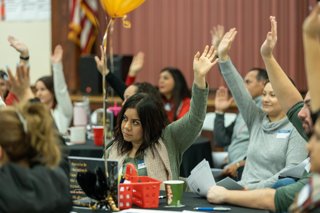 Room full of employees raise hands during staff development