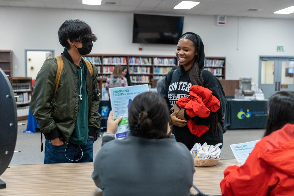 Seated student hands wellness materials to male and female students