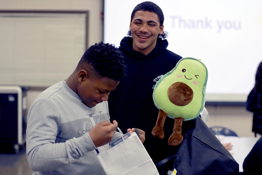 A student holds an avocado plush toy while another looks inside a goodie bag