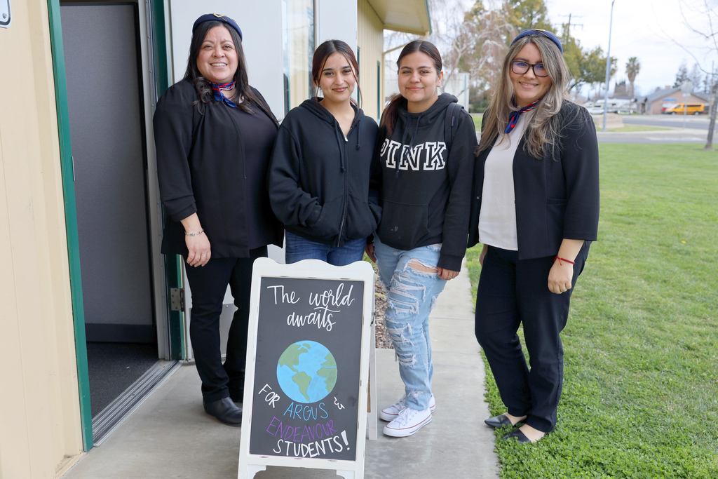 Two staff members and two students behind a sign that reads "The World Awaits"