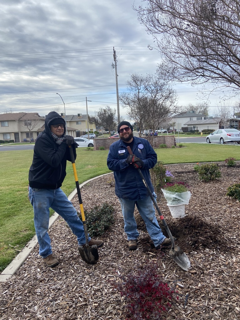 Two landscapers hold shovels while working in a flowerbed