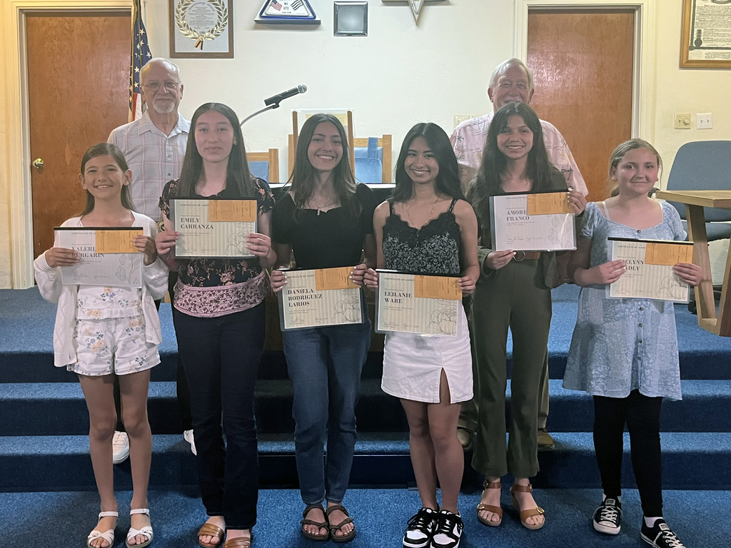 Five female students holding certificates, pictured with two Masons 