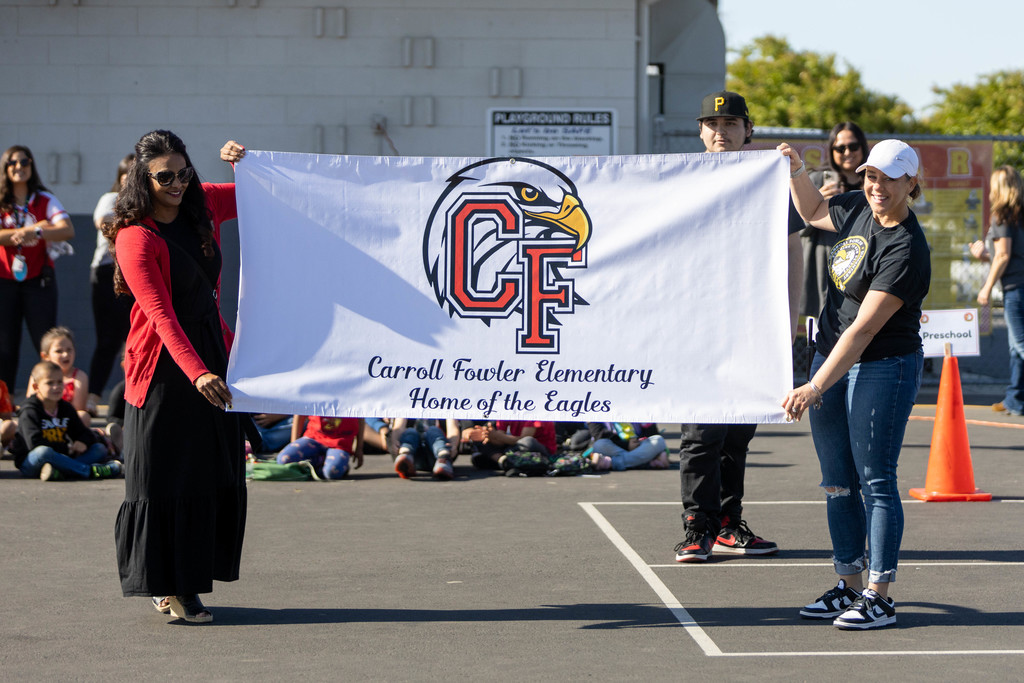 A banner depicting the new logo is displayed at a school assembly