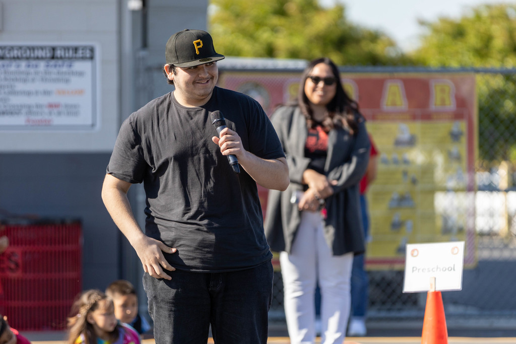 Logo designer Pedro Diaz holds micophone, addressing students at assembly