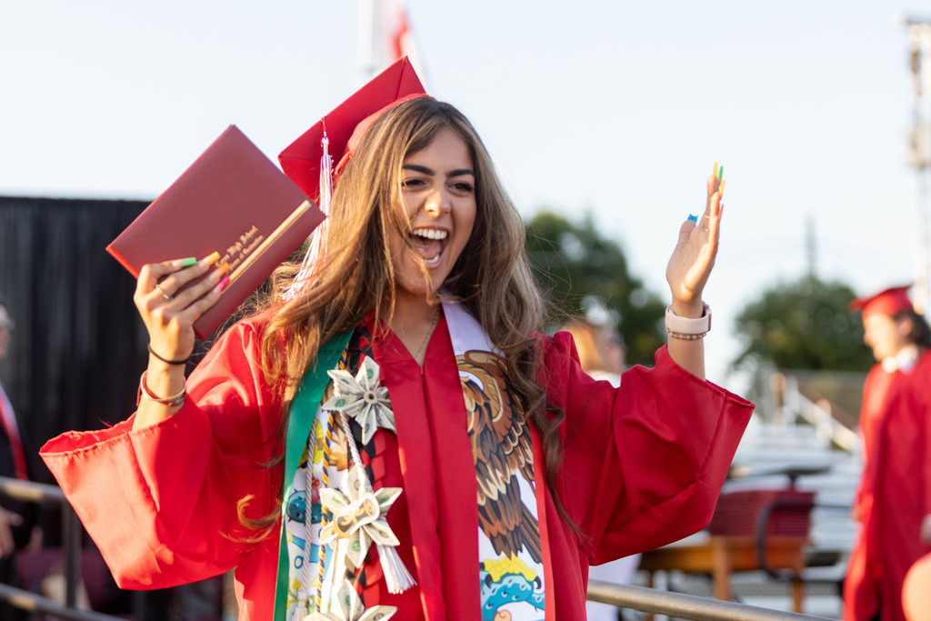 Female Ceres High School student in red cap and gown jubilantly holds up diploma