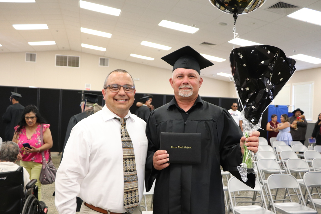 Adult Education student in cap and gown poses with instructor Bob Elms