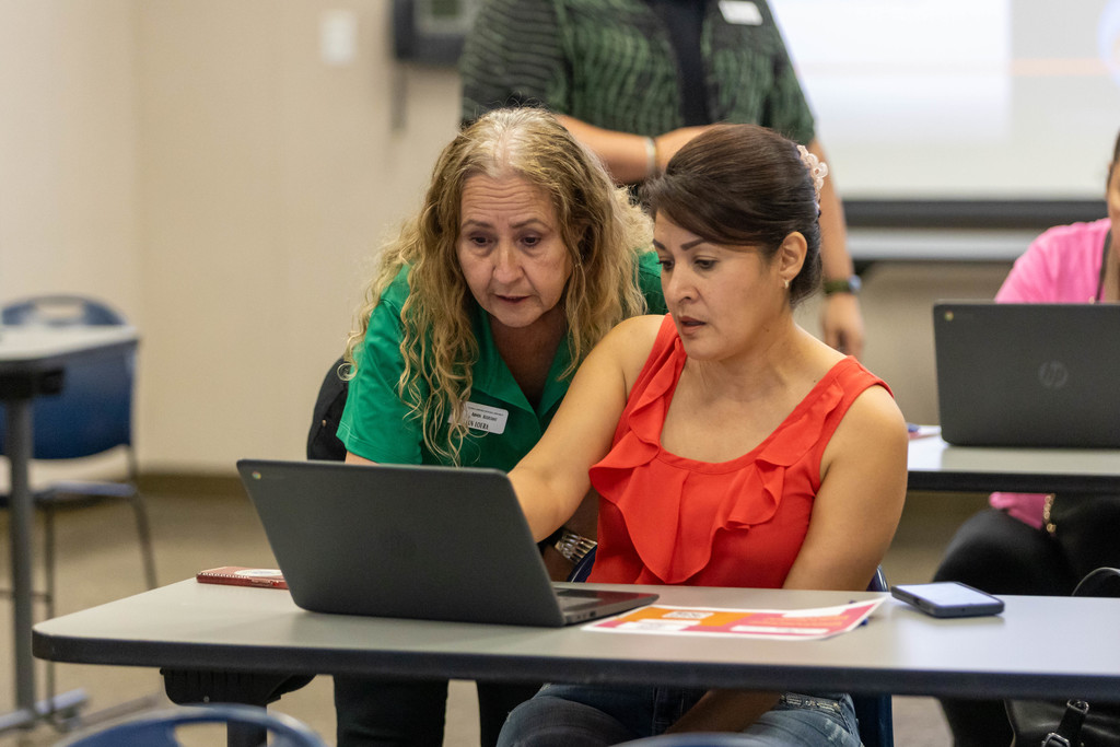 Staff member in green shirt looking at computer screen with parent
