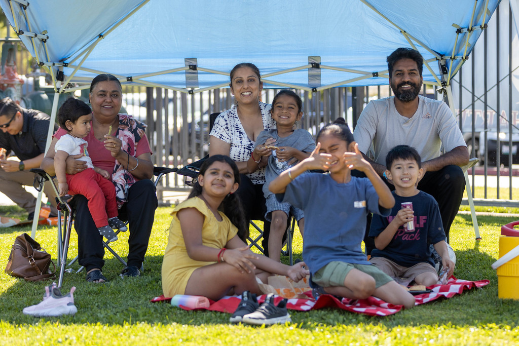 Family seated on lawn smiles for camera under blue canopy