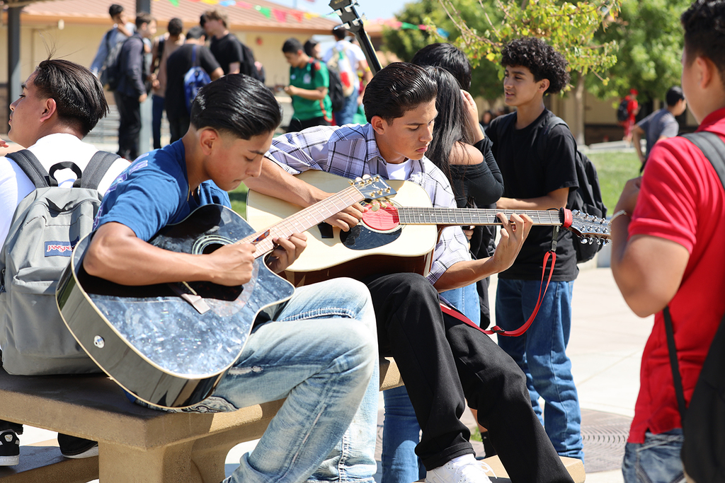 Two male students sit on bench playing guitars